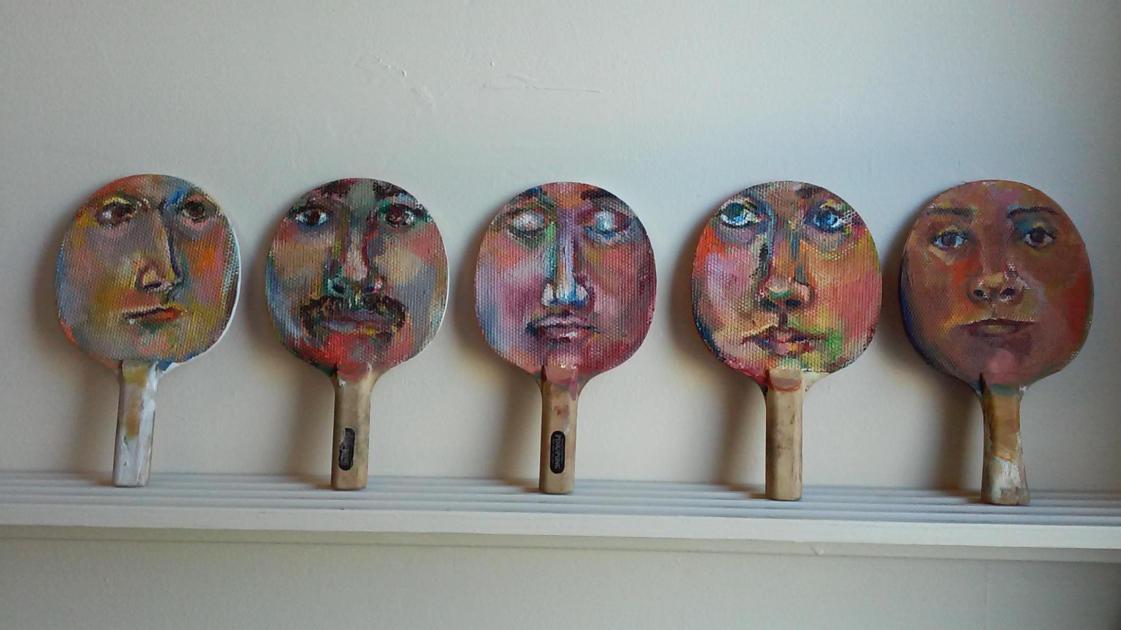 display of artistic faces painted on ping pong paddles