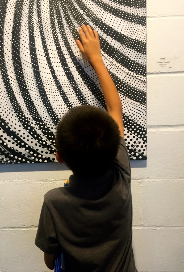 Child reaching up and exploring acrylic artwork by Judi Cain