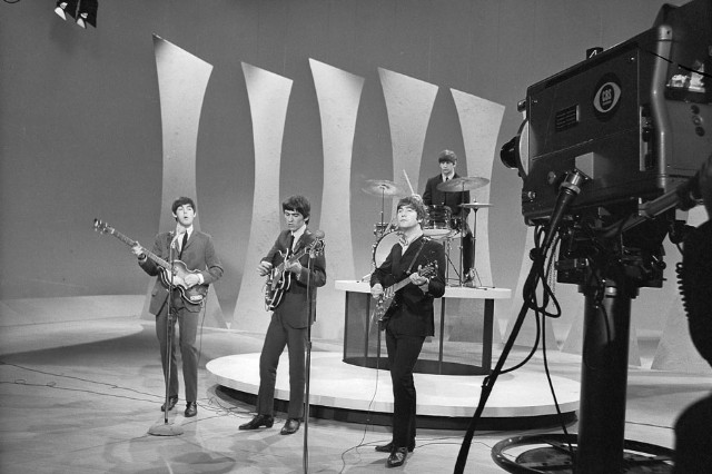 Historic image of the beatles performing on stage in front of tv camera