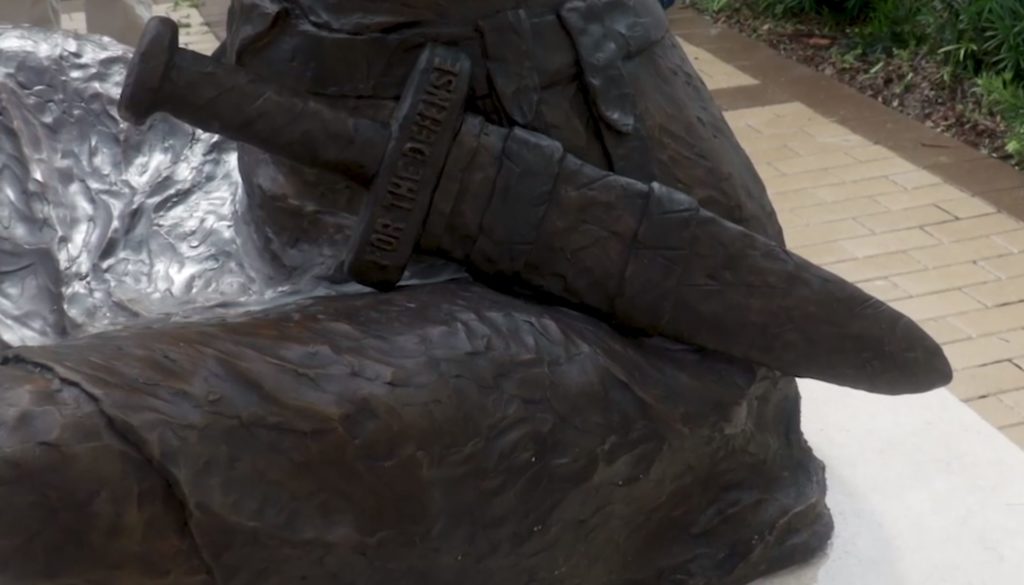 Close up of shethed sword with a visible inscription reading For The Defense