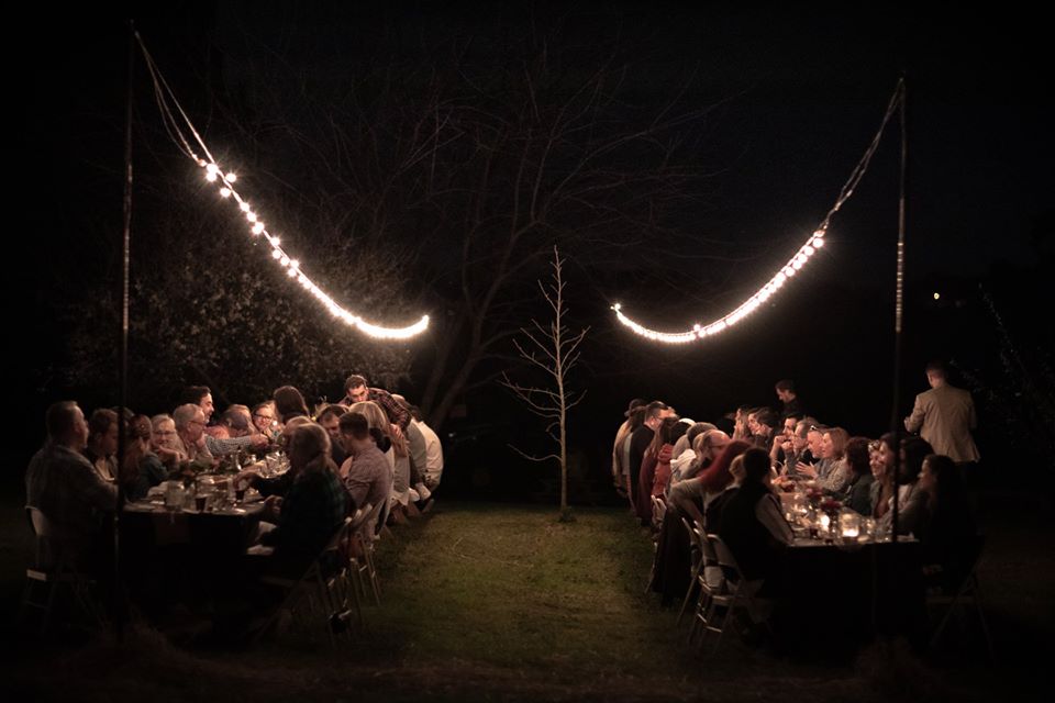 Diners sitting around tables on the grass under string lights