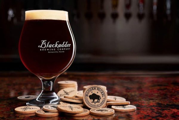 Beer in glass with logo of blackadder brewery and a pile of wooden nickels