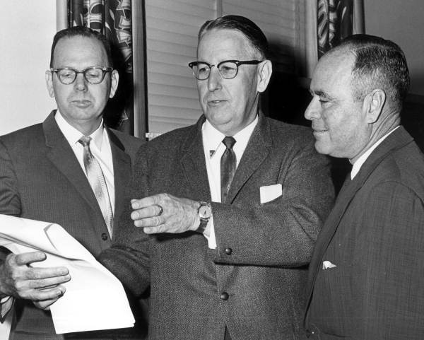 black and white photo of men looking at a sheet of paper