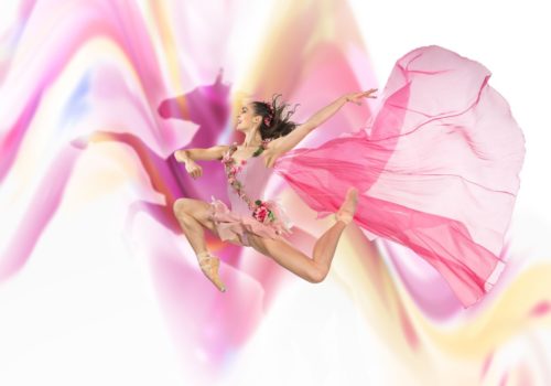 ballet dancer dressed in pink leaping in the air with the image of a horse behind her