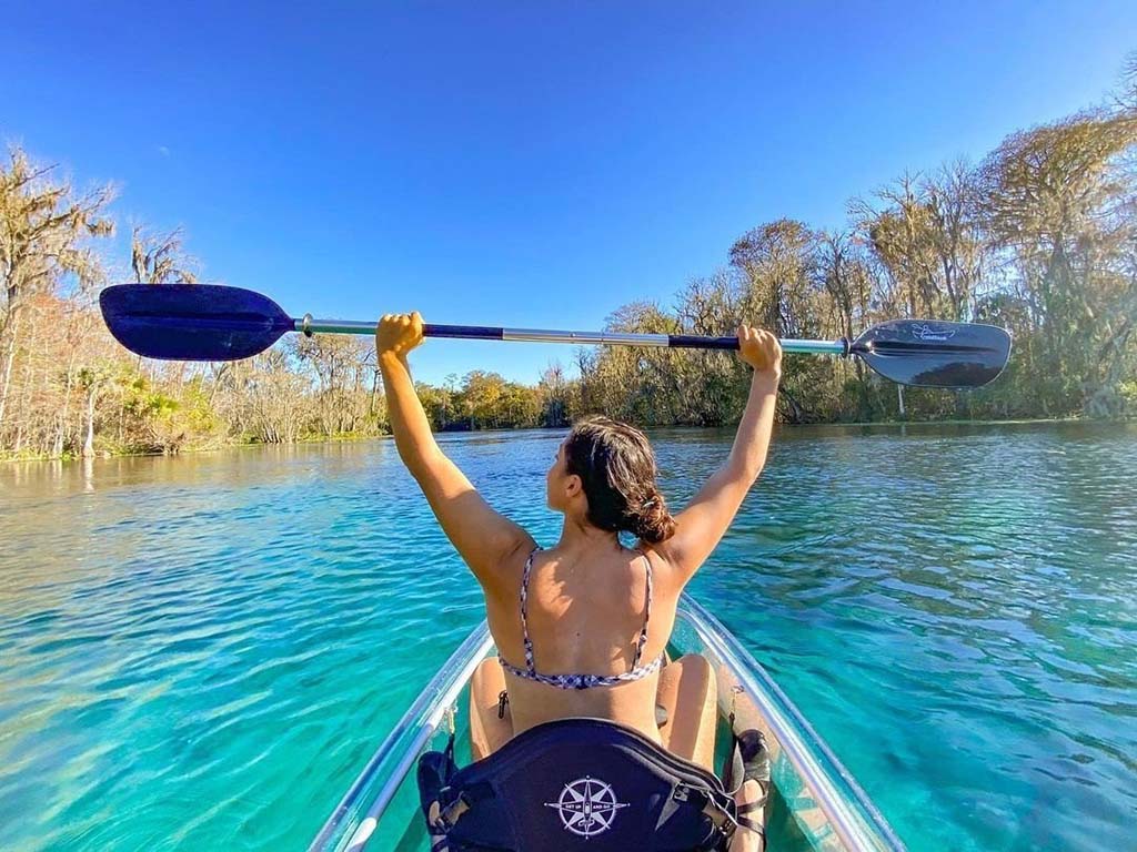 person in clear kayak holding up paddle