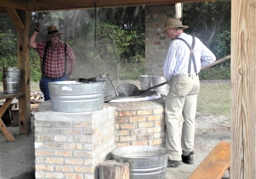 men in period dress boiling cane syrup