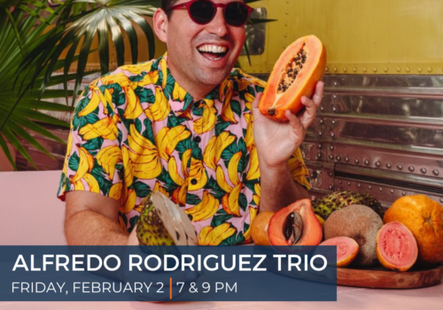 Image of Cuban pianist Alfredo Rodriguez in a bright shirt holding a papaya