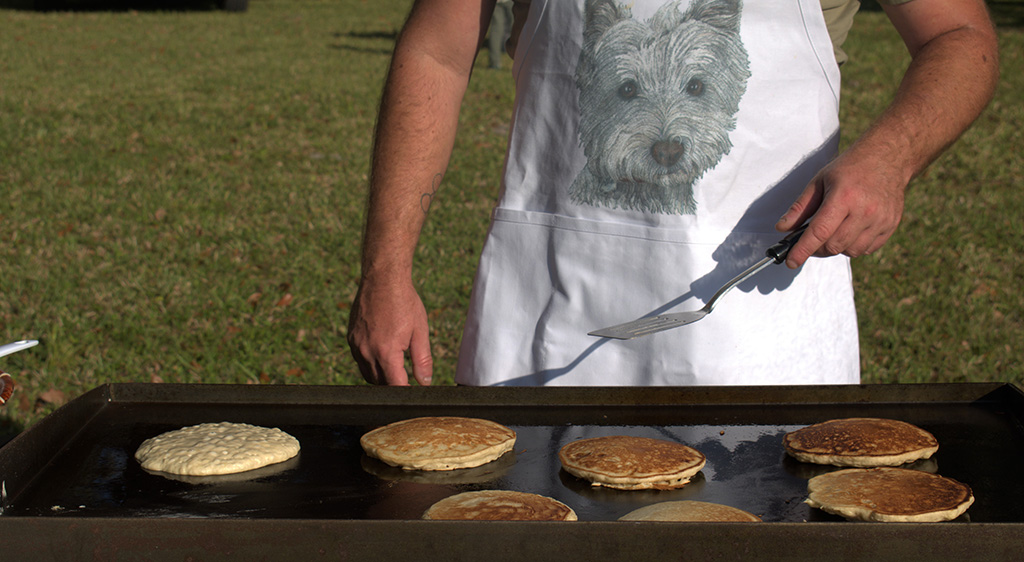 person cooking pancakes wearing an apron with a puppy print