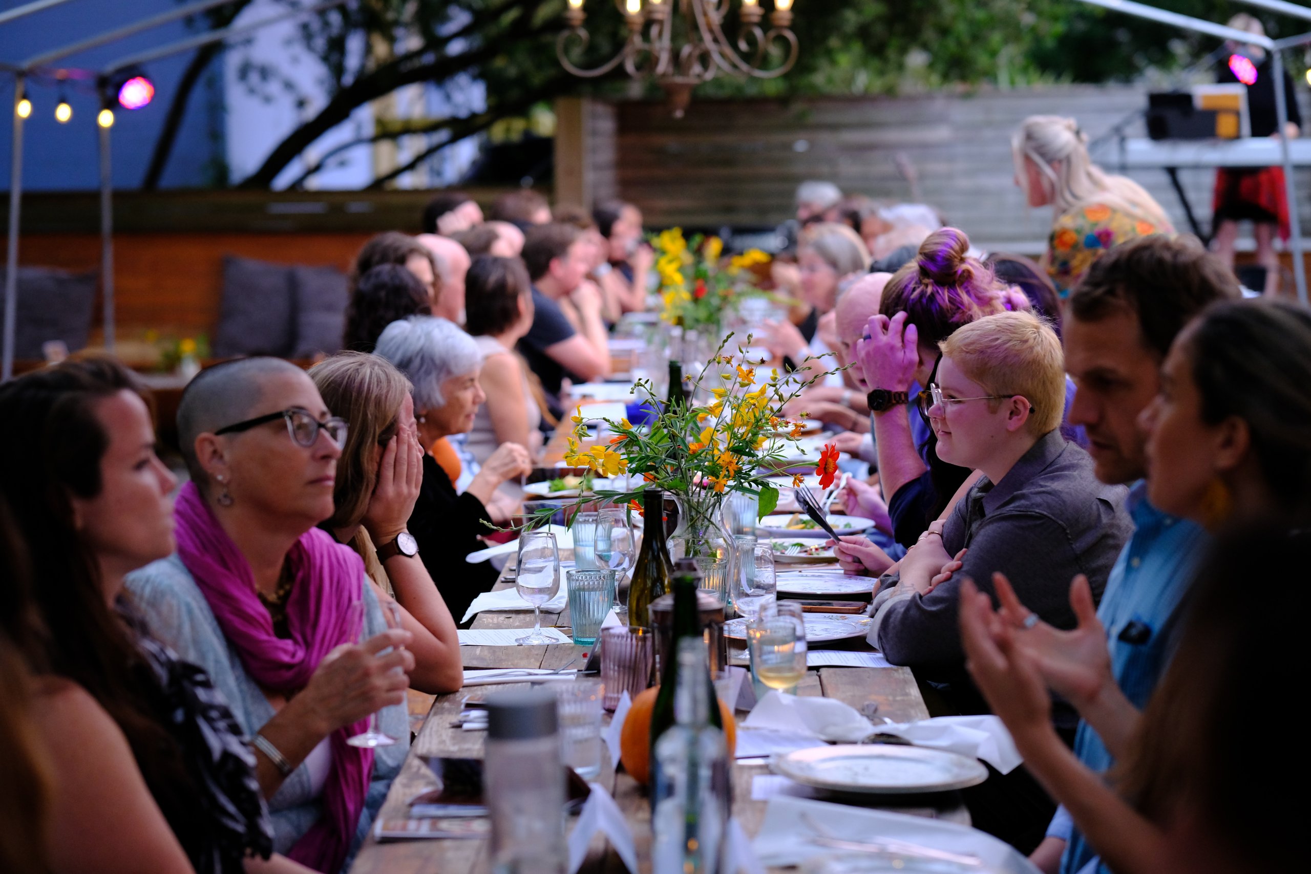 people sitting at a long table setting for a farm to table dinner