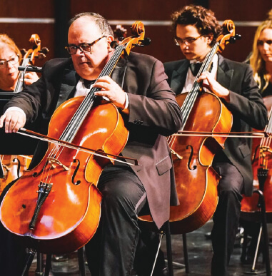 Gainesville Orchestra featuring their string section with men and women dressed in tuxedos. Parisian Nights