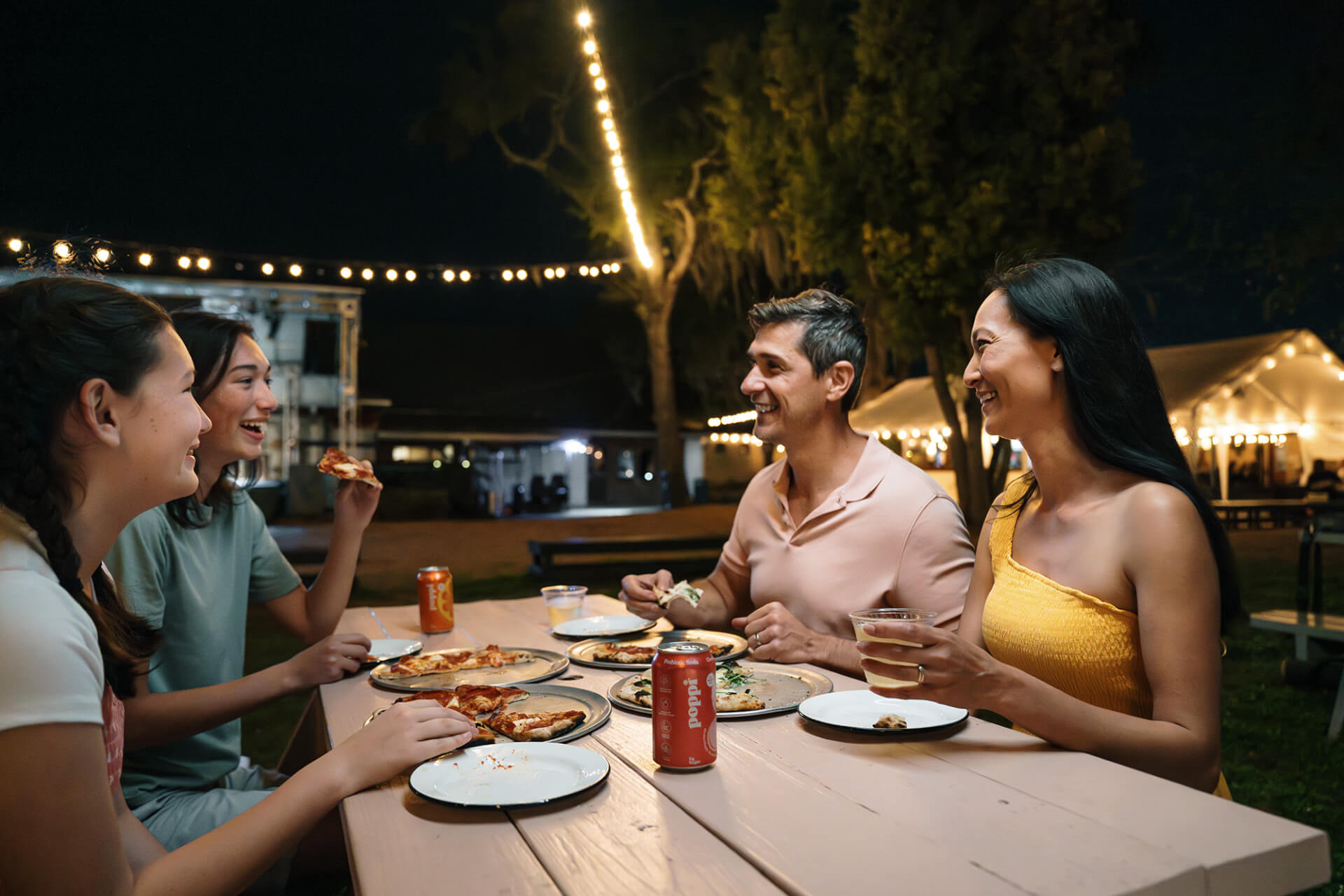 family smiling while dining outdoors under string lights