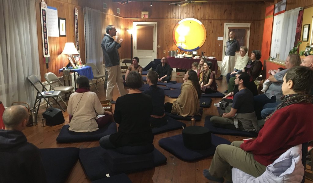 Several individuals of various backgrounds seated on floor cushions in a meditation room, participating in a group discussion.
