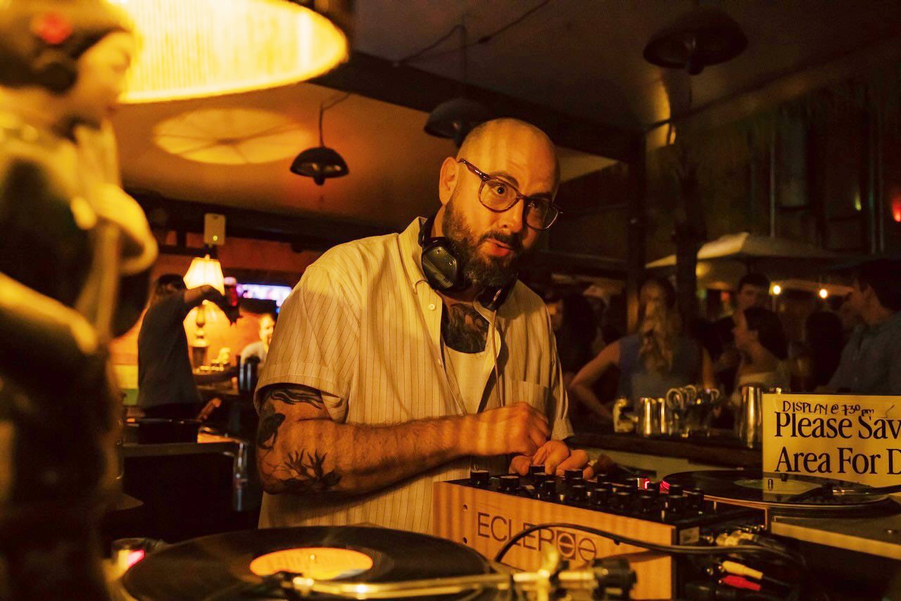 Art After Dark: DJ Pepito Von Dracula sitting at a turn table in a crowded bard.